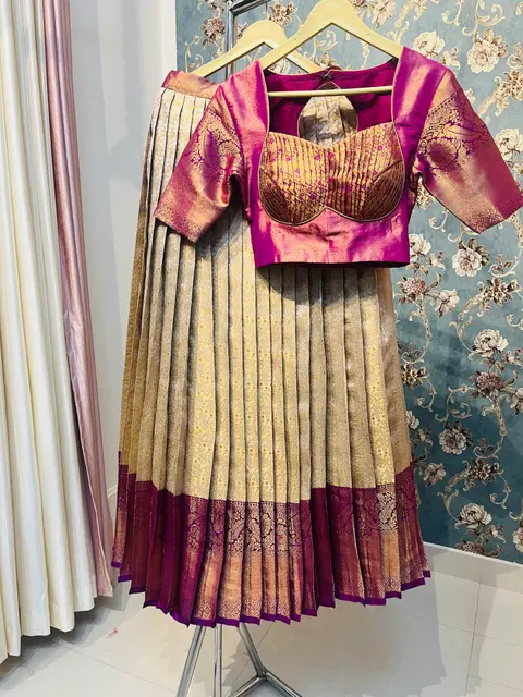 A magenta and gold brocade blouse over a cream and maroon pleated lehenga.