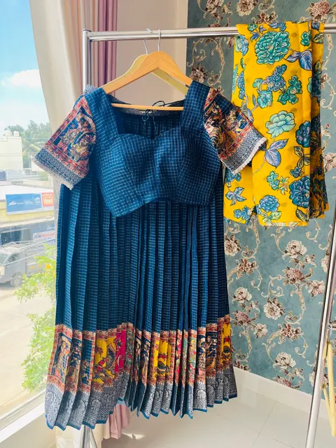 A teal checked blouse and a yellow kalamkari outfit hanging in the studio window.