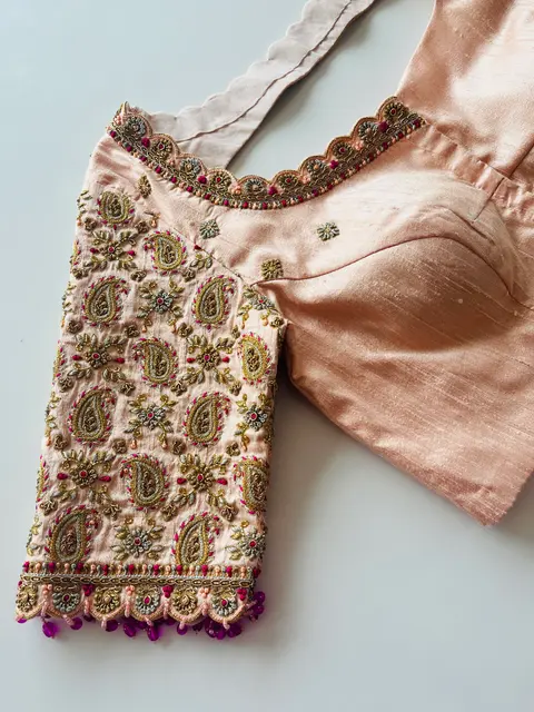 A blush and rose-gold blouse with paisley aari embroidery across the sleeve and shoulder.