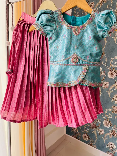 A pale blue blouse with an embroidered edge, beside a pink pleated skirt.
